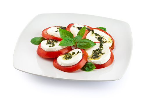 Arrangement of fresh mozzarella and tomatoes with basil and pesto on mozzarella top disposed on circular shape over a white plate isolated on white backdrop. Image includes an excellent clipping path on dishware.