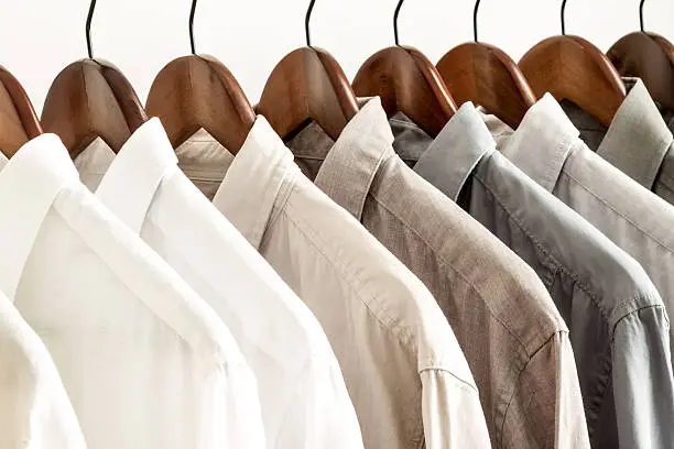 Photo of Row of white and beige shirts on wooden hangers 