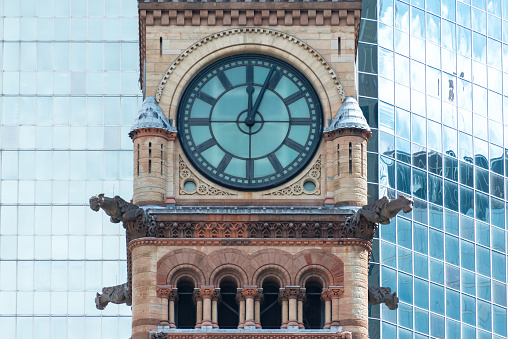 Architectural contrast: Old City Hall with a glass wall of a modern building as a background. Building was designed by Edward James Lennox in a variance of the Romanesque revival architecture called Richardsonian Revival.  The building is located at the corner of Queen and Bay Streets, across Nathan Phillips Square and the new City Hall. The heritage landmark has a distinctive clock tower which offers the culminating view.