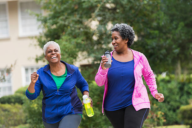 Two senior black women exercising together Two senior African American women getting in shape together.  They are jogging or power walking on a sidewalk in a residential neighborhood, talking and laughing. racewalking photos stock pictures, royalty-free photos & images
