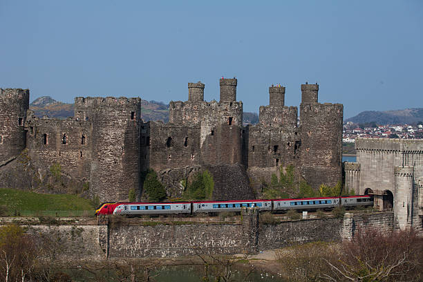 ligne ferroviaire, circule le long de la base de la medeval castle - conwy castle train travel people traveling photos et images de collection
