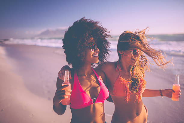 afro niña y su amigo caminando en la playa con alcopops - beach party friendship teenage girls fotografías e imágenes de stock
