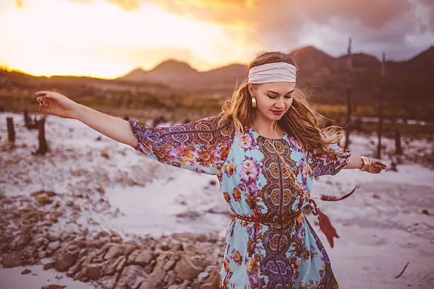 Boho girl dancing freely surrounded by nature in a floral dress on a golden summer evening