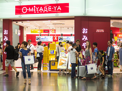Kyoto, Japan - August 11, 2014: Front view of Japanese shop for present called O-miyage-ya on train station in Kyoto. People are coming in and out; some are walking by with suitcases or big bags. On floor is light reflection of the people while on wall is written Omijage shop in roman letters and Japans writing.