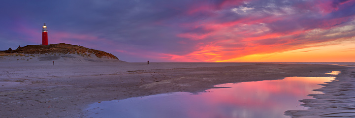 The lighthouse of the island of Texel in The Netherlands at sunset. Photographed from the beach below, with the sunset colours reflected in a tidal pool.