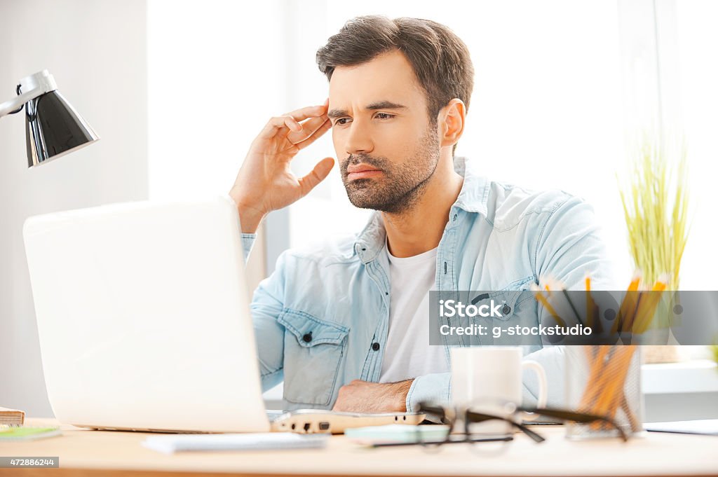 Concentrated on work. Handsome young man working on laptop while sitting at his working place 20-29 Years Stock Photo