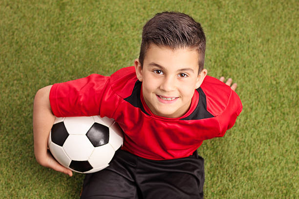 istock Junior football player sitting on grass and smiling 472888618