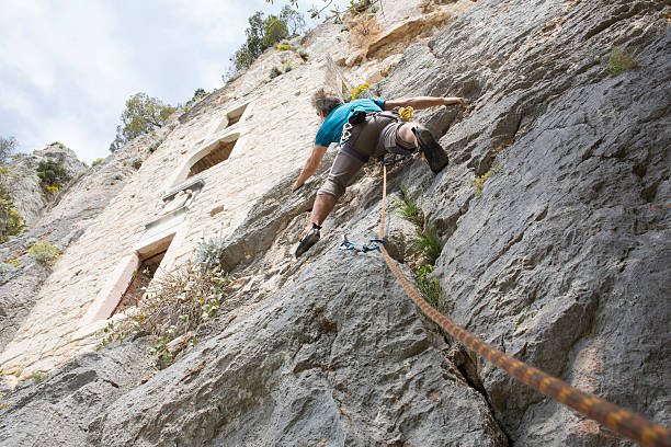 Rock climber ascends vertical cliff below historic stone dwelling