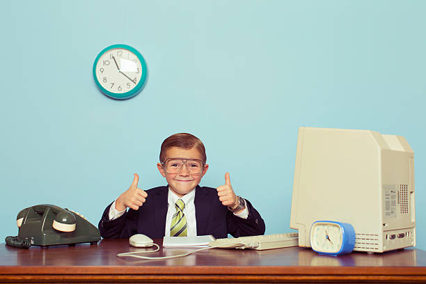 Young Boy Businessman Gives Thumbs Up at Office A young boy dressed as a businessman gives the thumbs up sign as there is some good business happening. He sits at his desk with retro computer and phone. super money stock pictures, royalty-free photos & images