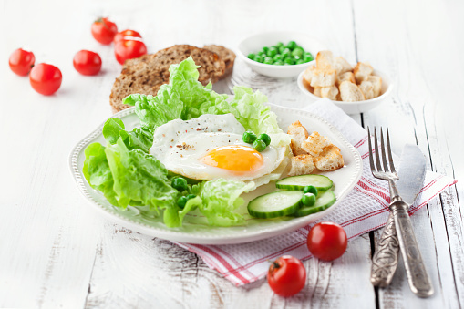 Breakfast with fried egg, vegetables and croutons on white wooden background, selective focus