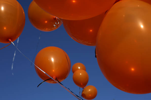 istock Clusters of Orange Balloons Floating on a Spring Day 472905542