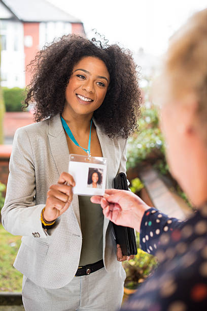 official door knocker at the door A young woman presents herself at the door of an elderly lady. She is dressed smartly and wearing a lanyard with official id and is showing it to the householder . The id badge has a photo and a blank space to add extra details. She is friendly and smiling. door to door salesperson photos stock pictures, royalty-free photos & images