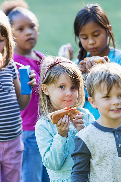 istock Little girl with group eating hotdog 472927106