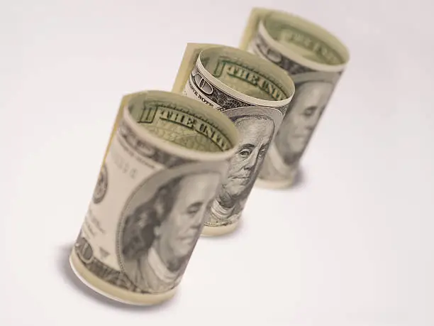 Three rolls of one hundred dollar bills on a white background.