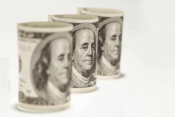 Three rolls of one hundred dollar bills on a white background.