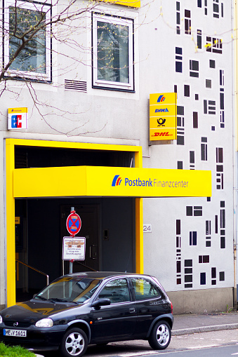 Ratingen, Germany - May 2, 2015: Postbank and DHL store in Germany. A car is parked in street.
