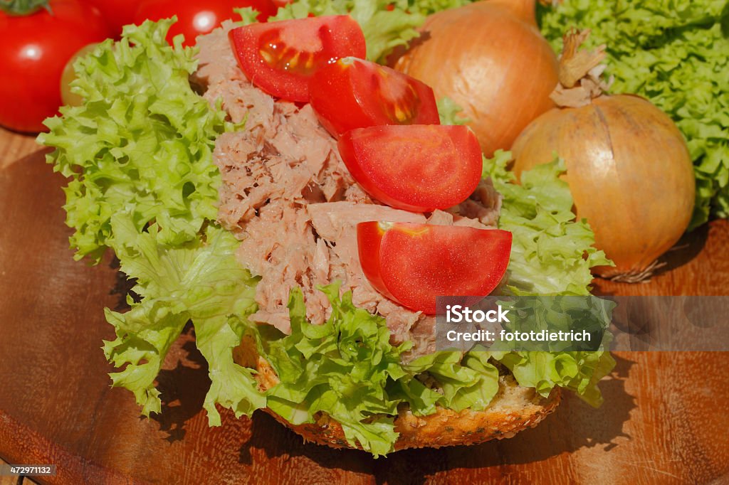 Fish rolls with tuna fillet garnished with lettuce Fish rolls with tuna fillet garnished with lettuce, tomato, onion and pickles on a wooden board 2015 Stock Photo