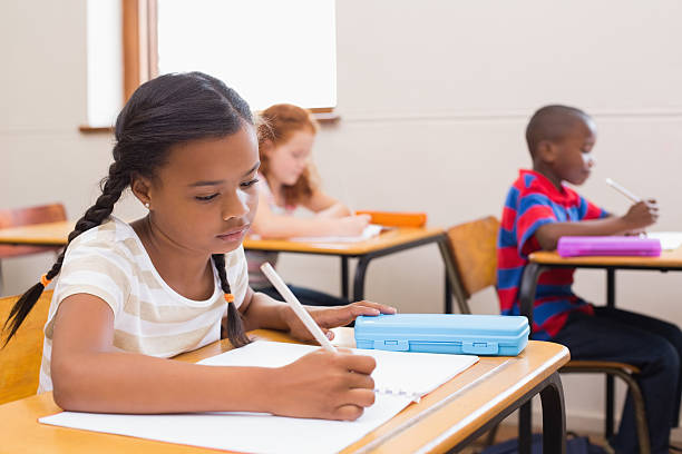 istock Cute pupils writing at desk in classroom 472974540