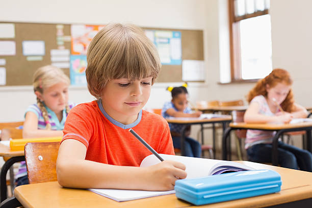 istock Cute pupils writing at desk in classroom 472974592