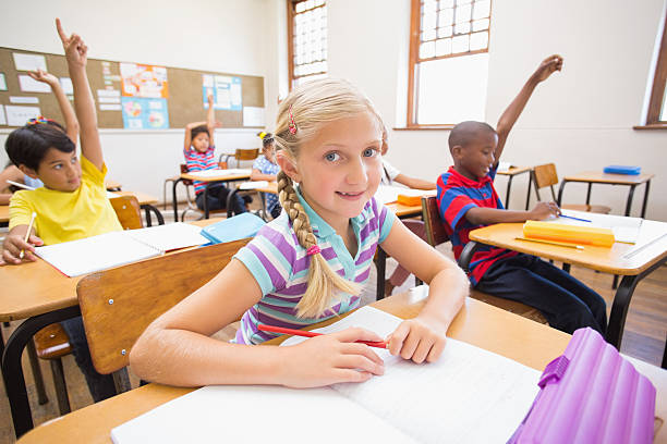 istock Cute pupil smiling at camera at her desk 472977058