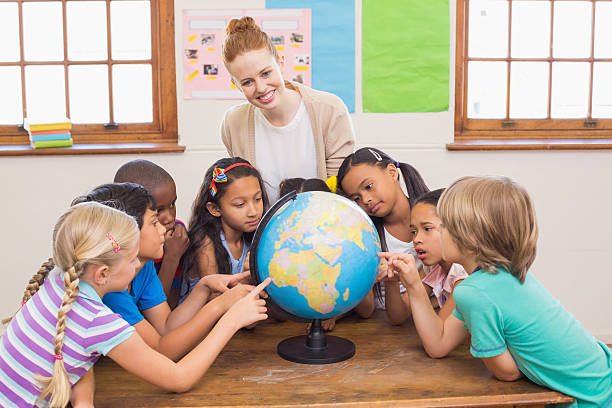 istock Cute pupils and teacher in classroom with globe 472977166