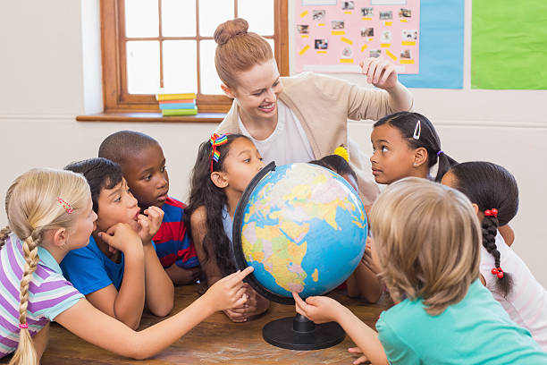 istock Cute pupils and teacher in classroom with globe 472977180