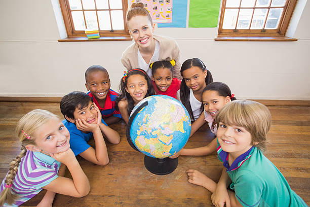 istock Cute pupils and teacher in classroom with globe 472977188