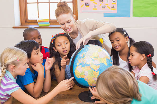 istock Cute pupils and teacher in classroom with globe 472977190
