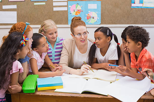 istock Teacher and pupils working at desk together 472977210