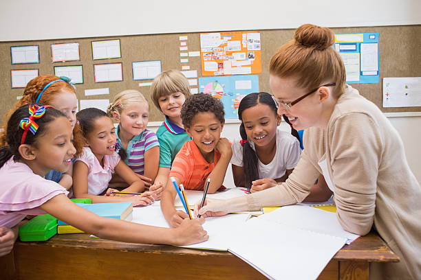 istock Teacher and pupils working at desk together 472977220
