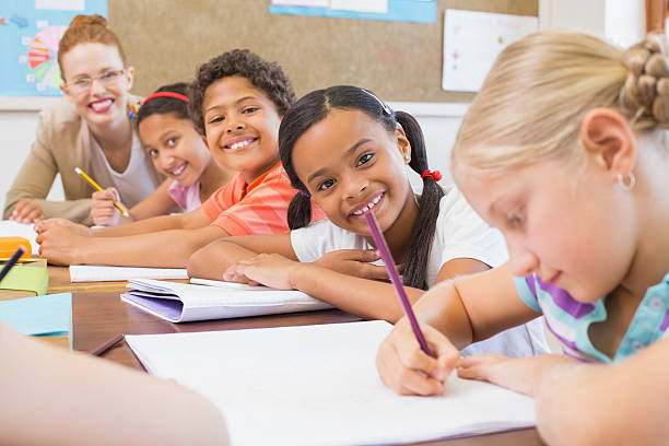 istock Cute pupils writing at desk in classroom 472977292