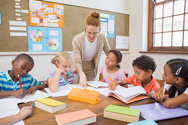 istock Pretty teacher helping pupils in classroom 472977296