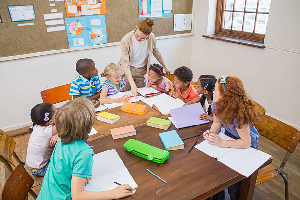 istock Pretty teacher helping pupils in classroom 472977298