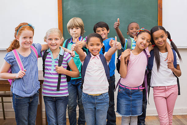 istock Cute pupils smiling at camera in classroom 472977598