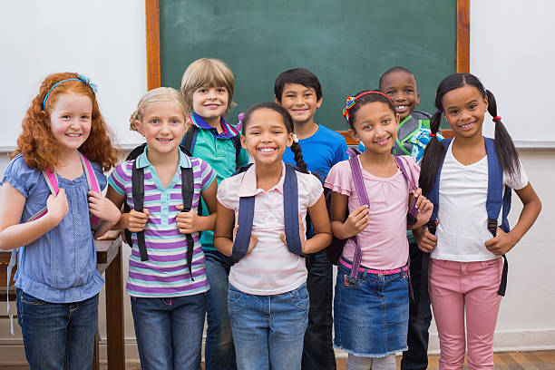 istock Cute pupils smiling at camera in classroom 472977600