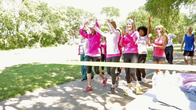 Large team of women crossing finish line during breast cancer awareness race for charity