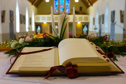 Open Bible and wedding flowers on the altar in catholic church. Shallow DOF