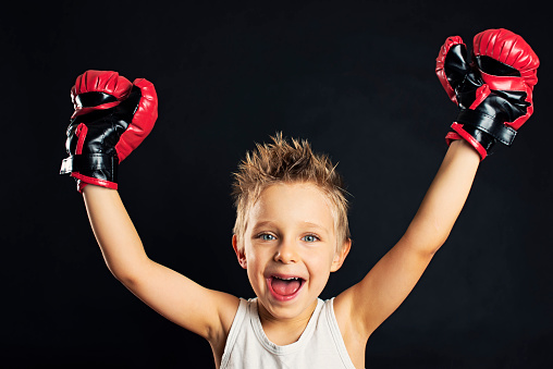 Little boy playing boxer rising arms in gesture of victory. The boy is aged four and is smiing into the camera with joy.