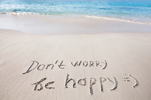 Don't worry, be happy - words on the sand on paradise beach