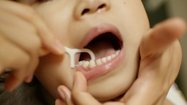 mom clean teeth for kid with floss, closeup,shallow DOF.
