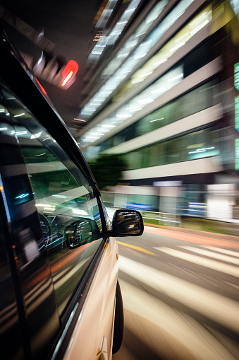 A car drives through the brightly lit Shibuya area of Tokyo, Japan at night. Taken with a remote mounted camera on the exterior of the moving car.