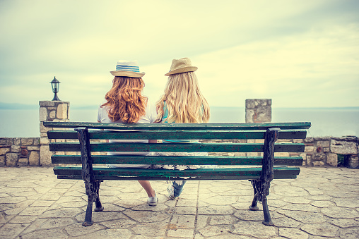 Best friends with straw hat sitting on a bench by the sea