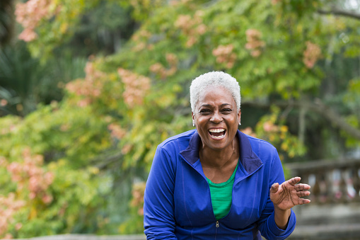 Portrait of a senior, African American woman at the park with an excited expression on her face.  She is looking at the camera, laughing.