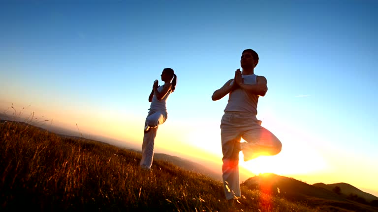 HD1080p: Super Slow Motion CRANE shot of a couple practicing yoga outdoors on the ridge at sunset. Recorded at 1050 fps.