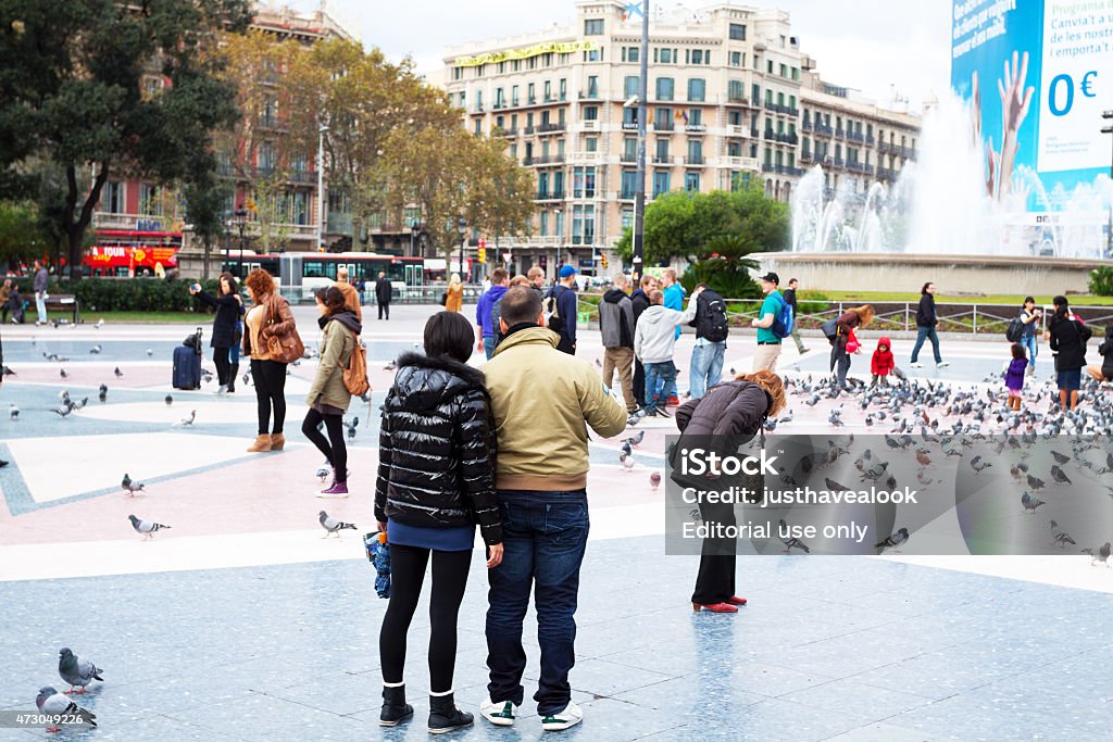 Asian tourist couple on Placa de Catalunya Barcelona, Spain - November 22, 2011: An Asian tourist couple is watching people and architecture on square Placa de Catalunya in Barcelona. Many people are passing on square. In background are buildings. 2015 Stock Photo