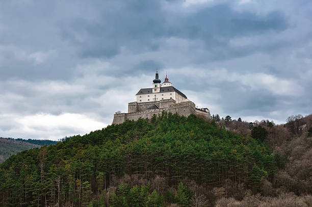 A medieval stone castle with a Turkish flag on top, set against a bright blue sky in a mountainous region.