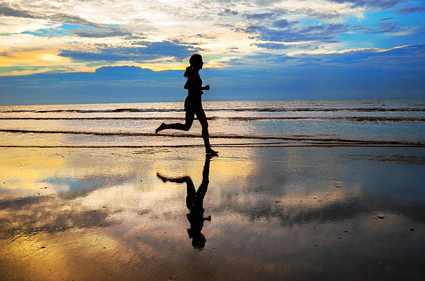 istock Silhouette of woman jogger running on sunset beach with reflection 473057392