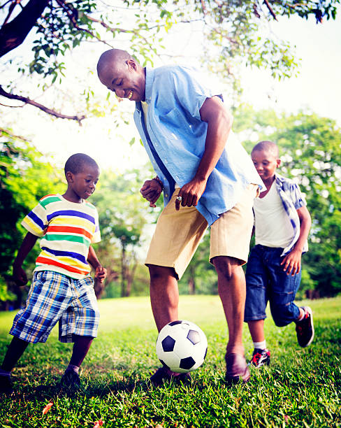 istock Black man and two black boys playing with a ball on grass 473057904