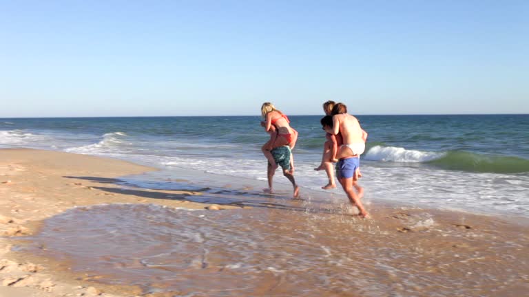 Group Of Teenage Friends Having Piggyback Race Along Beach Together