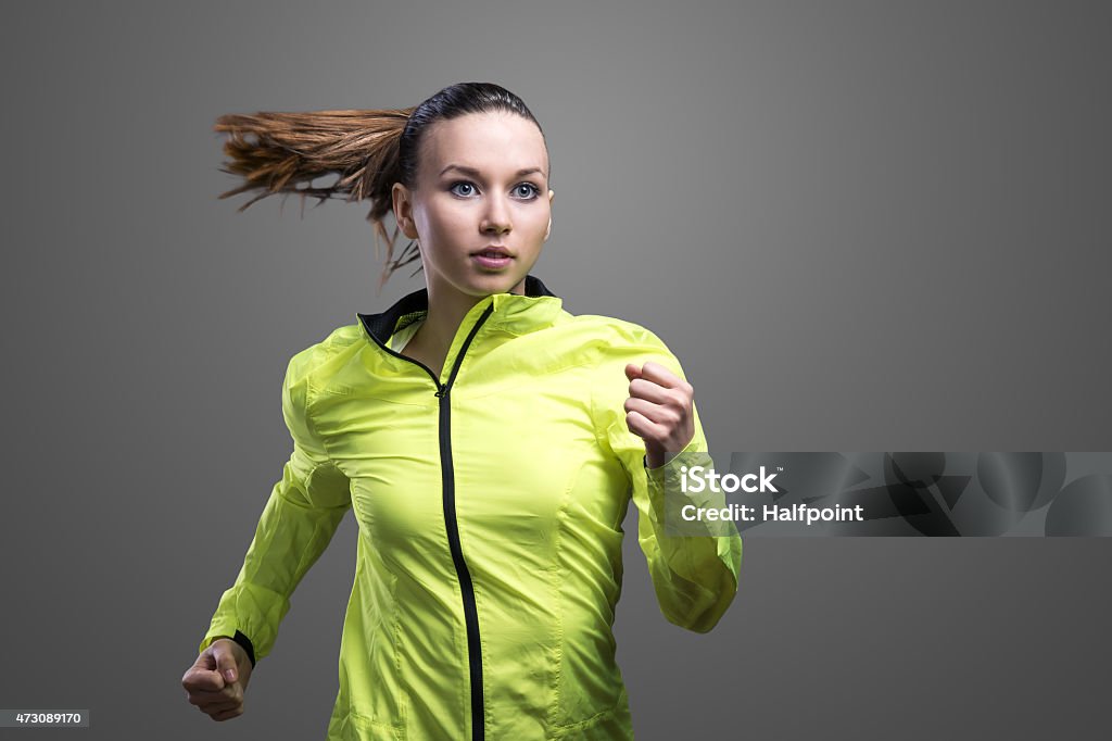 Beautiful woman runner in green jacket Young beautiful woman running. Studio shot on gray background. Jacket Stock Photo